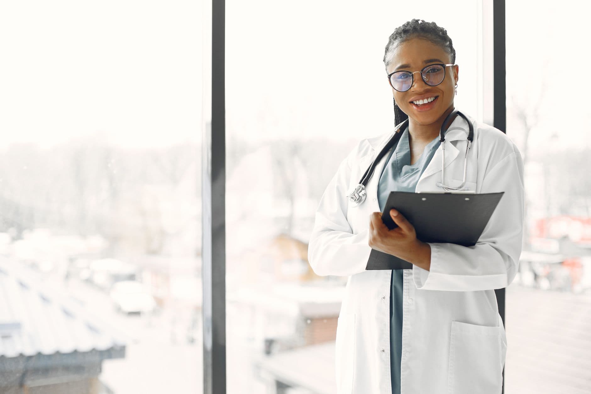 Confident female doctor in a white coat holding a clipboard in a bright hospital setting.