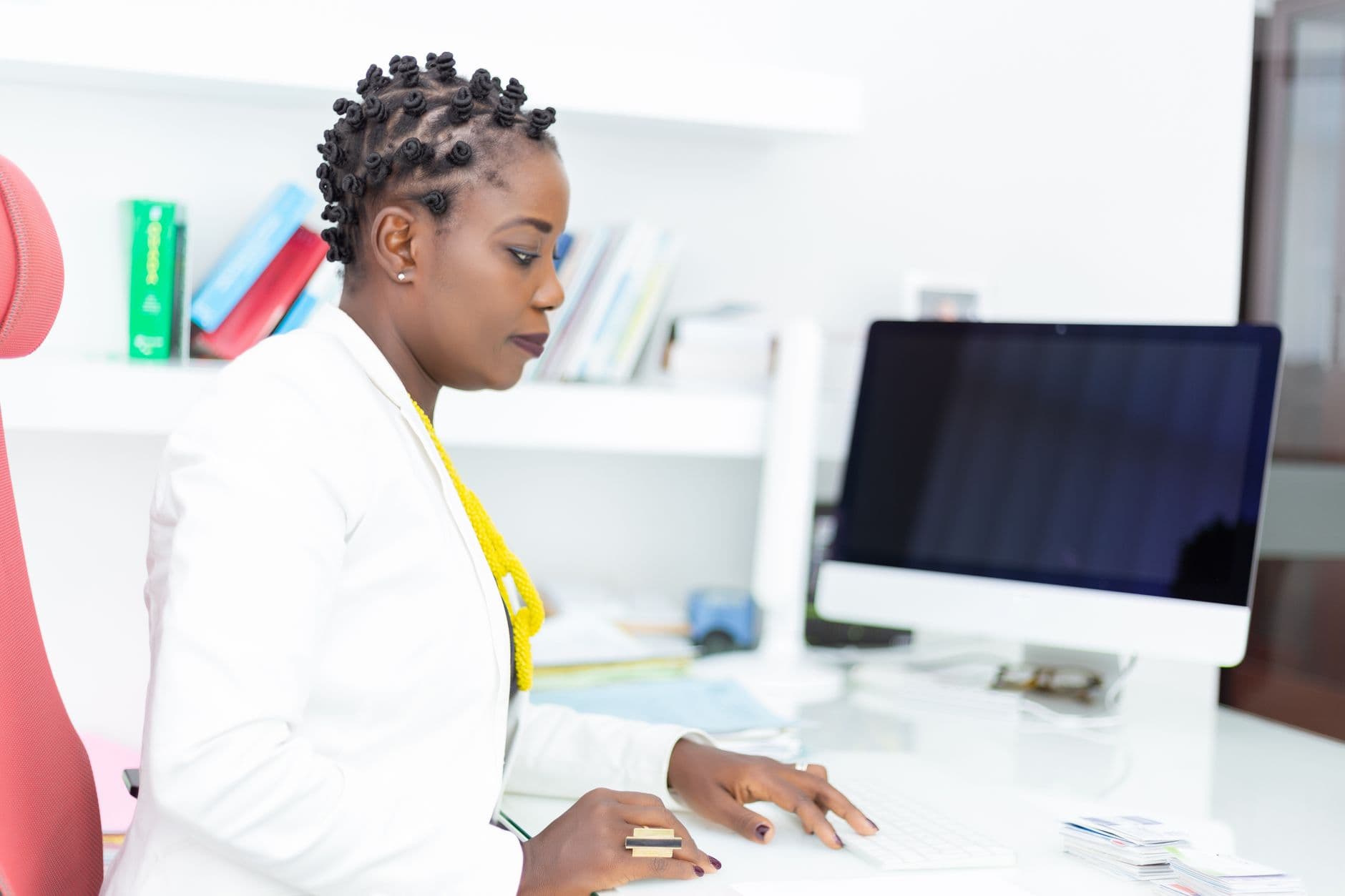 African woman with bantu knots working at a computer desk in a modern office setting.